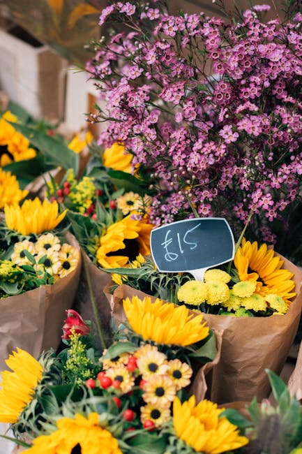 A vibrant display of fresh floral arrangements at a flower market, featuring bright yellow sunflowers with large, open petals and prominent dark centers, alongside smaller white and yellow daisies. Th